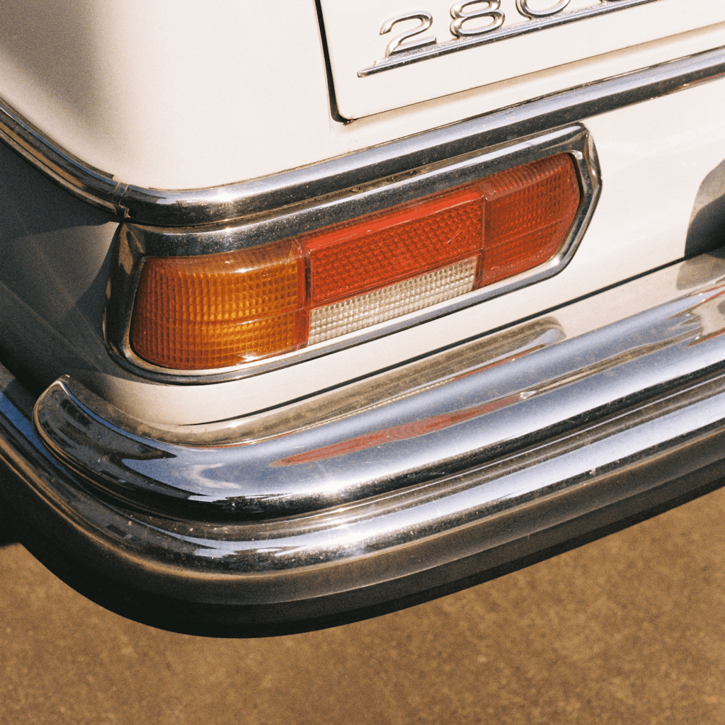 Close-up of the rear corner of a vintage cream-colored car, filling most of the frame at a slight downward angle.