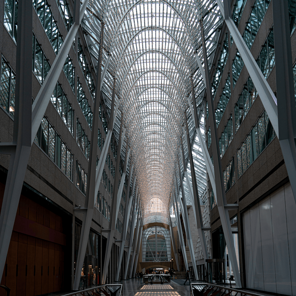 The scene is set indoors within a spectacular architectural atrium, characterized by a high, vaulted glass ceiling arching above, allowing natural light to filter in.