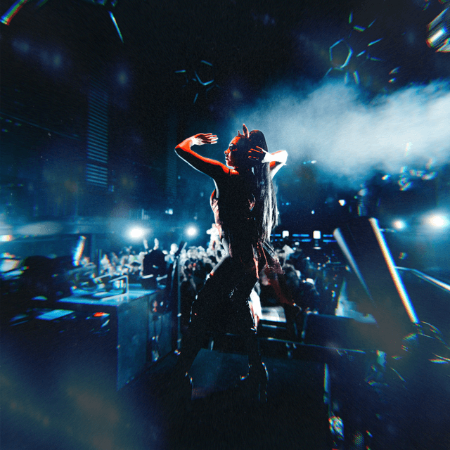 The scene takes place indoors, in what appears to be a dimly lit nightclub or concert hall.