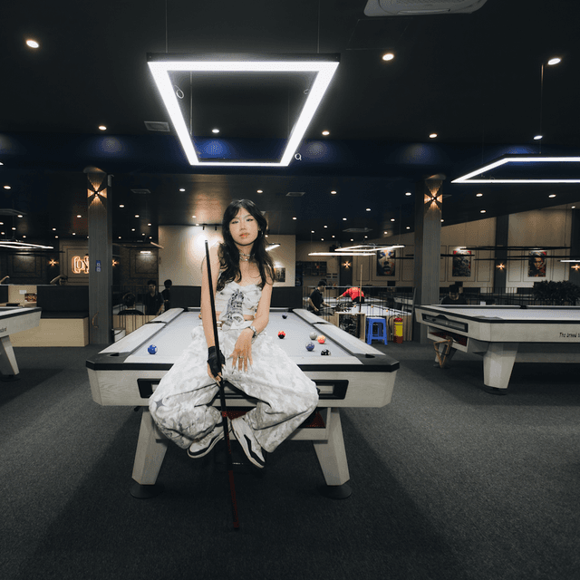 The scene is set indoors, in a modern billiards hall illuminated by bright, artificial lighting.