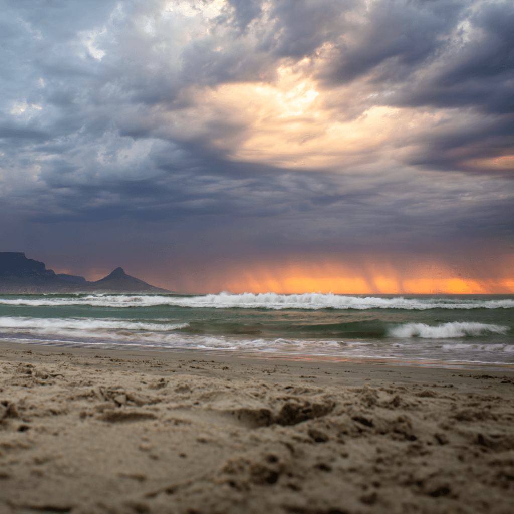 The scene is set outdoors on a sandy beach, likely during the evening as the sky is painted with a dramatic display of colors from the setting sun.