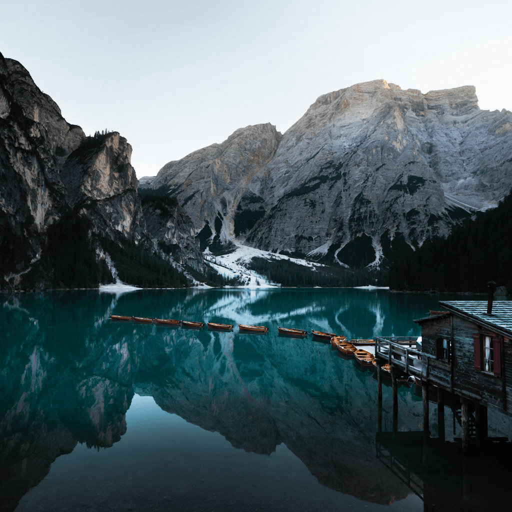 The scene is set outdoors, showcasing a tranquil lakeside landscape framed by towering, rugged mountains.