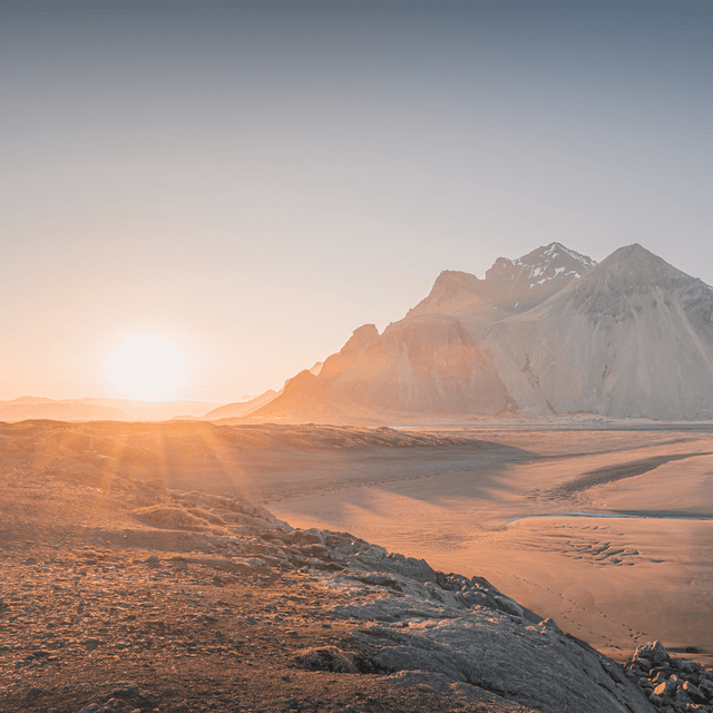 The scene unfolds outdoors at the base of a majestic mountain range during the serene hour of dawn.