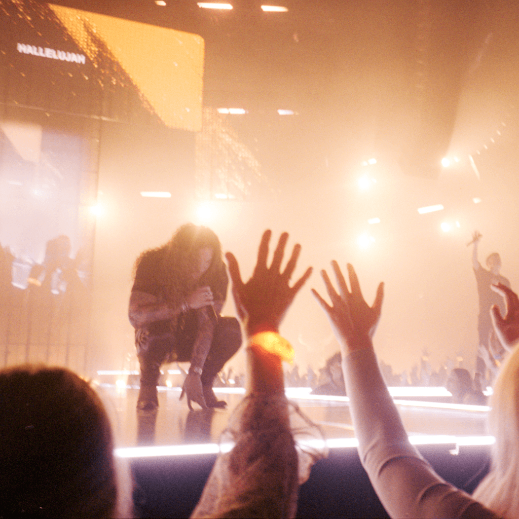 The scene is set indoors in a large, vibrant concert hall filled with energy.