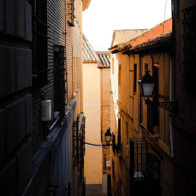 The scene is set in a narrow outdoor alleyway flanked by tall buildings, suggesting a charming, historical district.