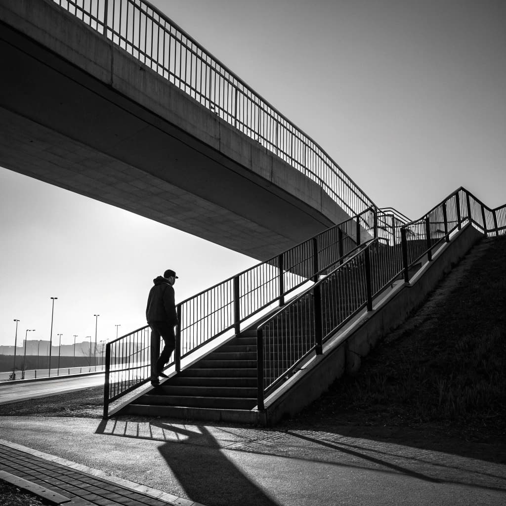 The scene is set outdoors, captured in stark black and white, with a modern architectural element—an overpass—imposing diagonally across the frame.