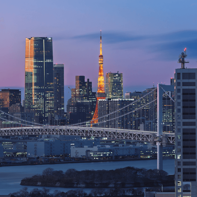 The scene is an outdoor cityscape at dusk, with the sky transitioning from deep blue to shades of purple and pink as the day turns to night.