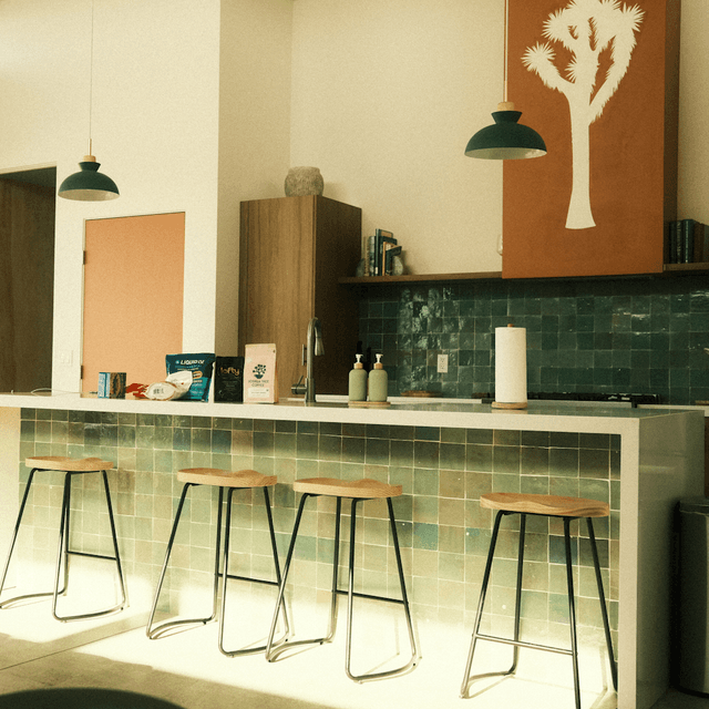 The scene depicts an indoor kitchen area filled with warm, late-afternoon light streaming through unseen windows, casting soft shadows across the space.