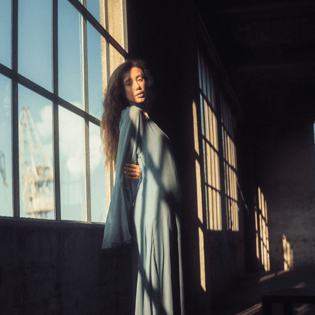 The scene is set indoors, possibly in a spacious industrial building or loft with large grid-style windows that stretch from floor to ceiling.